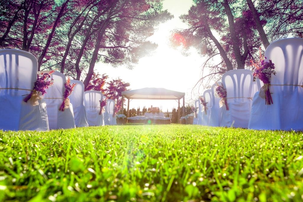 Wesele w plenerze – najpiękniejsze zakątki Śląska na romantyczną uroczystość ślubną 3 Udekorowane krzesła ustawione w rzędach na zielonej trawie prowadzące do altanki, gotowej na ceremonię ślubną w plenerze, oświetloną promieniami zachodzącego słońca. Idealna lokalizacja na ślub pod gołym niebem.